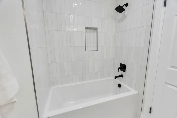 Bathtub and shower combination featuring vertical white subway tile, a built-in shower niche, and matte black fixtures