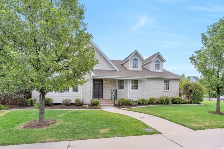 Traditional style residence featuring a light brick exterior, dormer windows, a covered entry, and mature landscaping