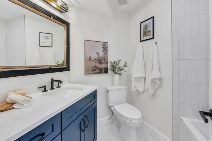 Bathroom featuring a navy blue vanity with a white countertop and rectangular sink, matte black faucet, framed mirror, and hexagonal floor tiling