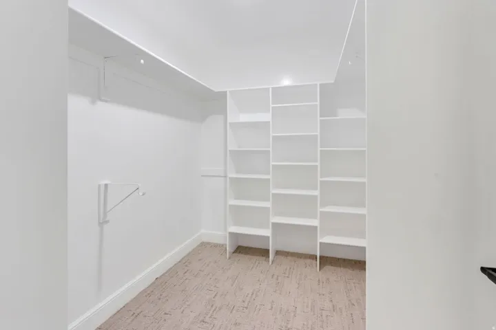 Dedicated closet space featuring white built-in shelving, white walls, white trim, and patterned carpeting