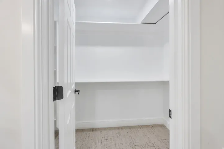 Recessed closet with white panel door, dark hardware, light wood-finish flooring, and multiple white shelving units