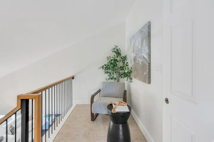 Upper landing area featuring a wood-finish handrail with black metal balusters, light-colored textured carpeting, and white walls