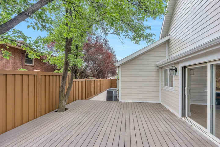 Spacious composite deck with integrated tree, featuring siding exterior, brown privacy fencing, and sliding glass door access