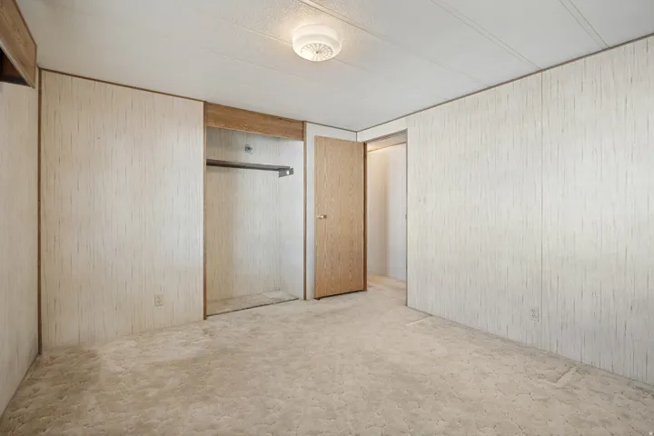 Carpeted interior space featuring light-toned panel walls with wood trim, a built-in closet with hanging rod, and a flush-mount ceiling light fixture