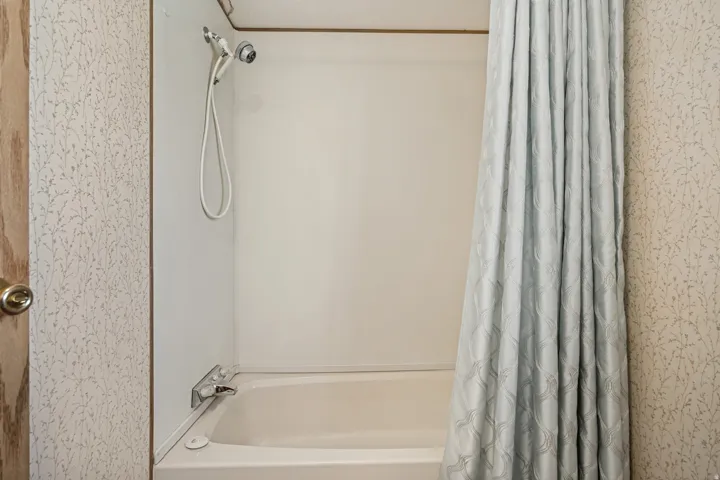 Bathtub with integrated shower surround, featuring a chrome shower head with handheld attachment and wall-mounted faucet