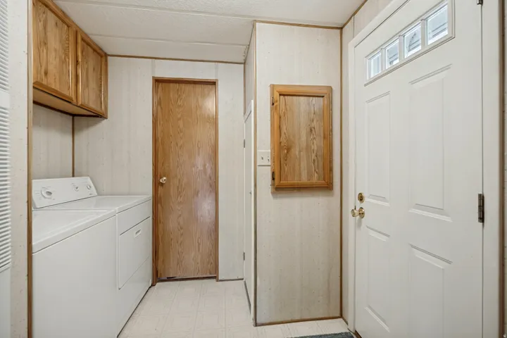 Laundry area featuring wood-finish cabinetry, light-toned wall paneling, and a white exterior door with decorative lites