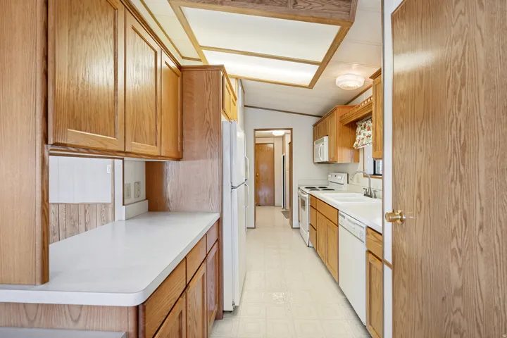Kitchen featuring wood-finish cabinetry, white countertops, and white appliances