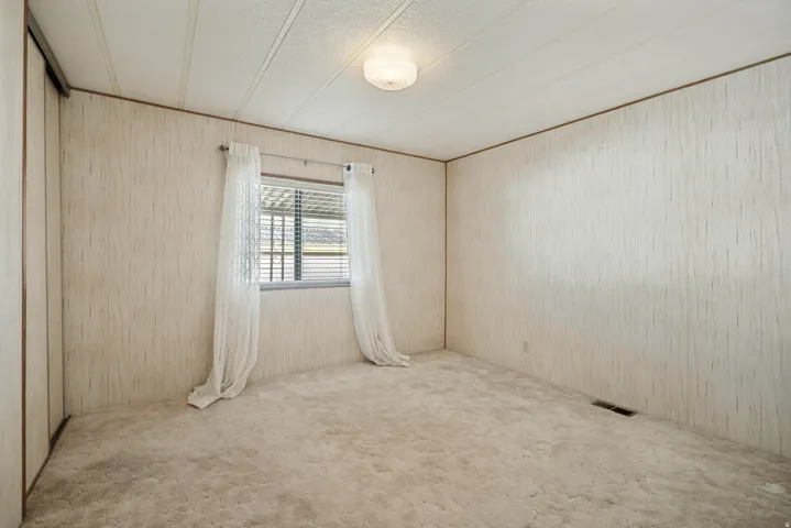 Carpeted room featuring a window with horizontal blinds and sheers, a ceiling-mounted light fixture, and textured wall finishes