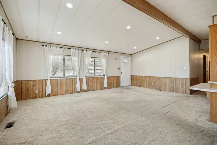 Spacious living area featuring light-colored carpeting, white paneled walls with wood-finish wainscoting, and recessed ceiling lighting