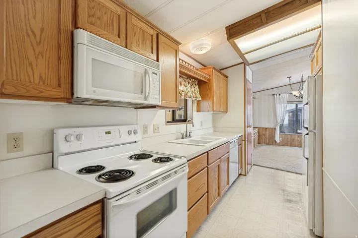 Kitchen featuring wood cabinetry, white countertops, dual basin sink, white electric range with overhead microwave, and vinyl flooring