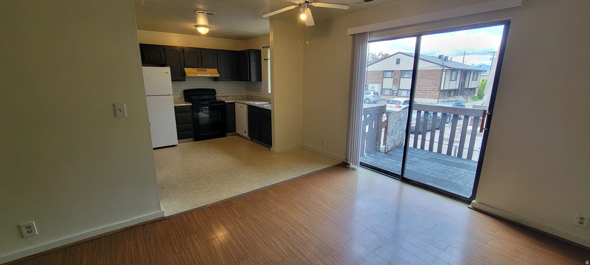 Open-concept living area featuring wood-finish flooring, a ceiling fan, and a kitchen with dark cabinetry