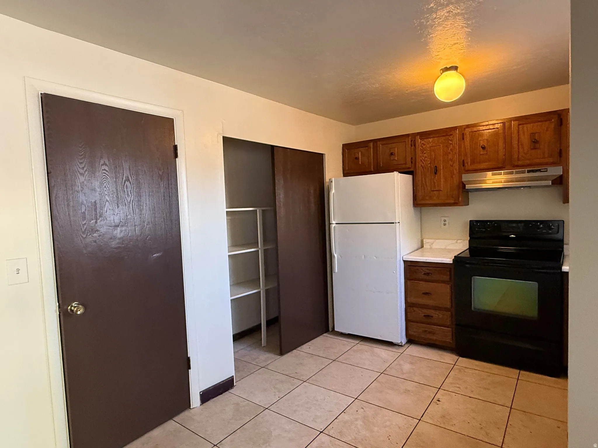 Kitchen featuring wood-finish cabinetry, white countertops, tile flooring, and a built-in pantry with shelving