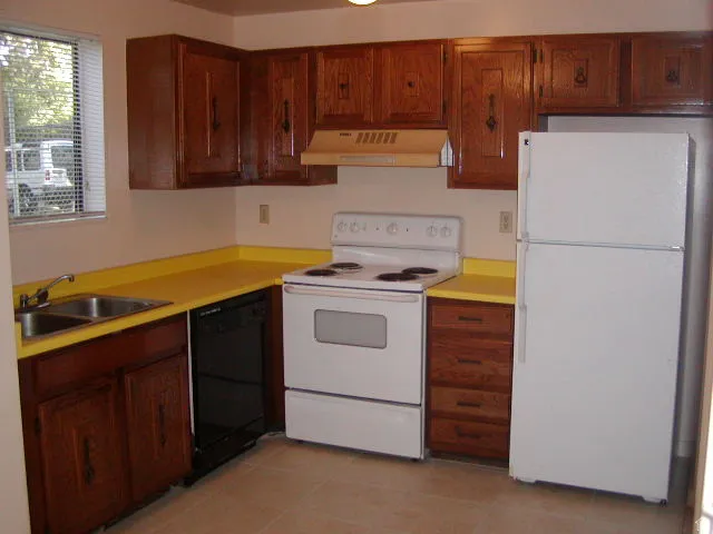 Kitchen featuring wood cabinetry, yellow countertops, a dual-basin stainless steel sink, and white appliances