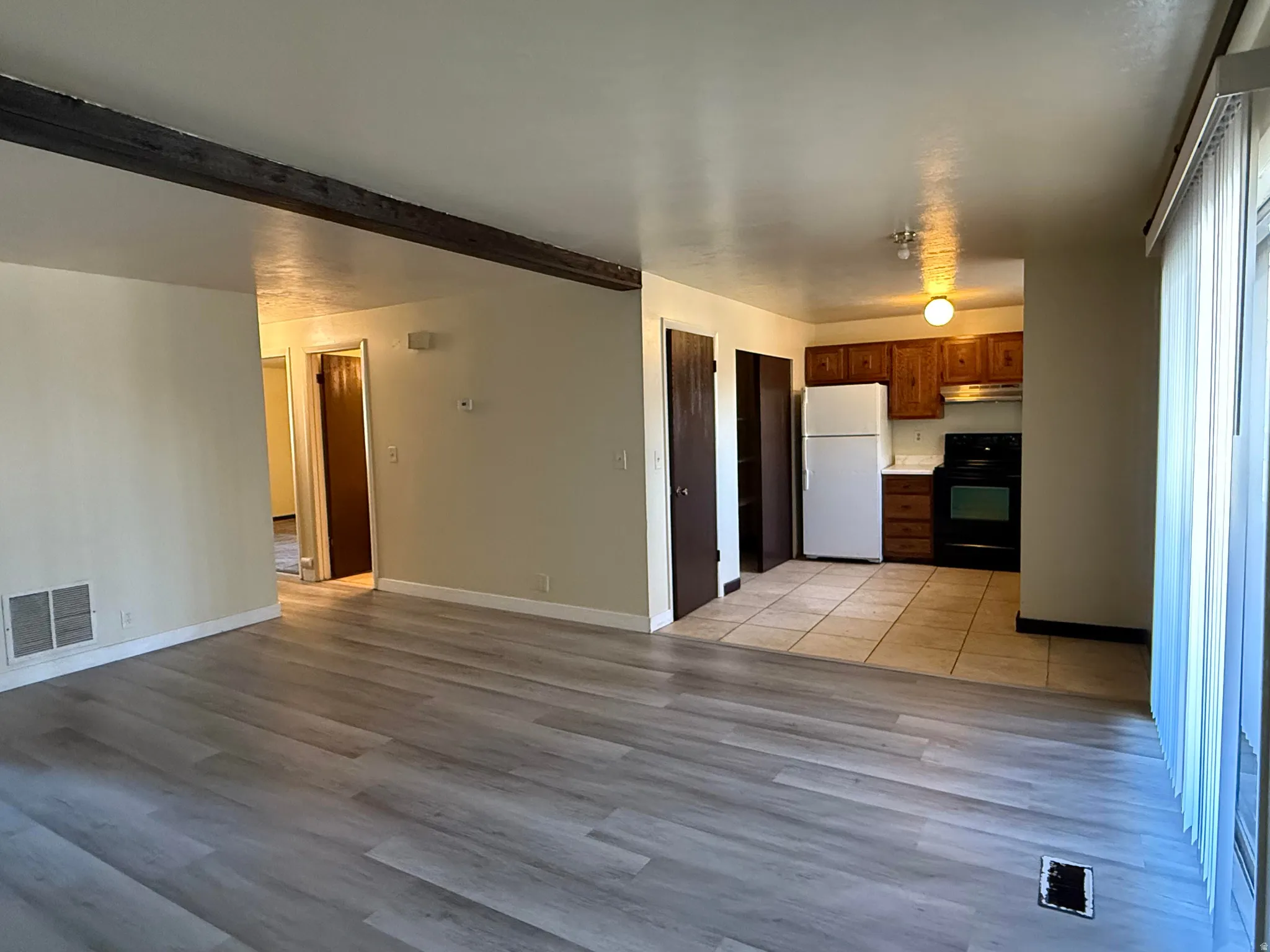 Spacious living area featuring wood-finish flooring, a decorative ceiling beam, and neutral wall tones
