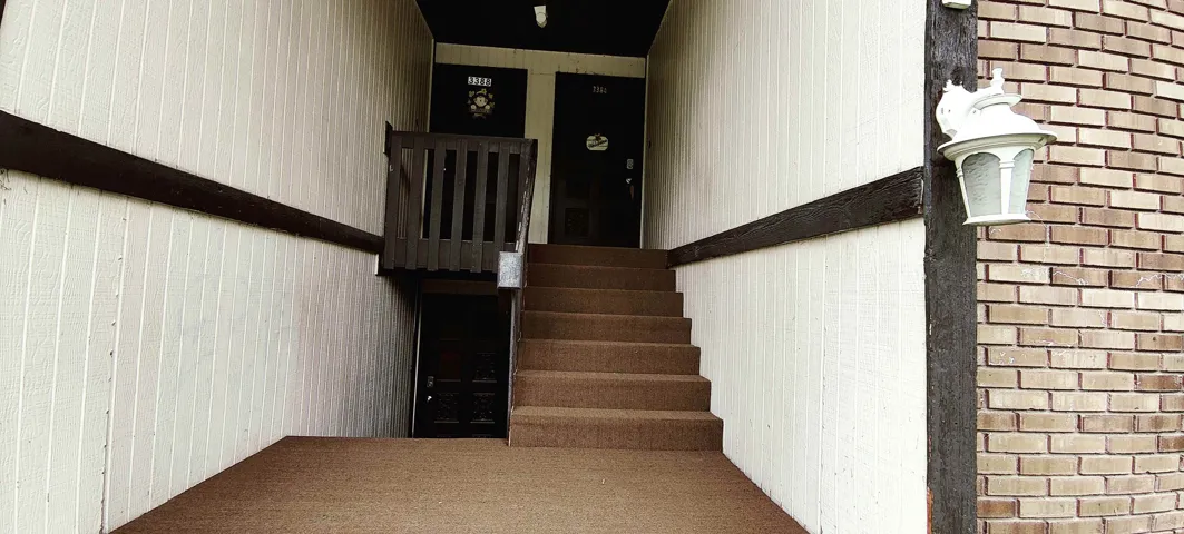Carpeted staircase with dark wood railings and accent beams