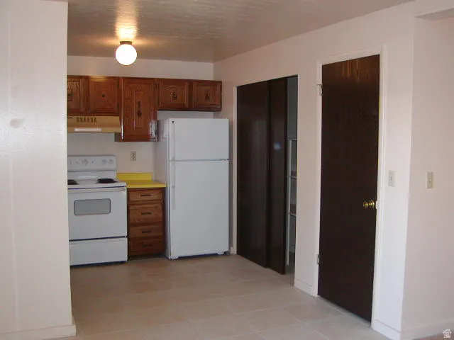 Kitchen area featuring wood-finish cabinetry, a white refrigerator, and a white electric range with an overhead vent