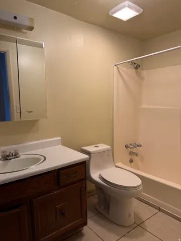Bathroom featuring a full-size bathtub with shower, a vanity with wood-finish cabinetry, a white countertop with integrated sink, a wall-mounted medicine cabinet, and tile flooring
