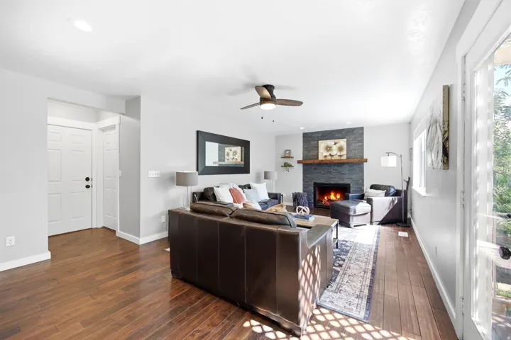 Living area featuring wood-finish flooring, a stacked stone fireplace with a wood mantel, a ceiling fan, recessed lighting, and a glass-paneled exterior door
