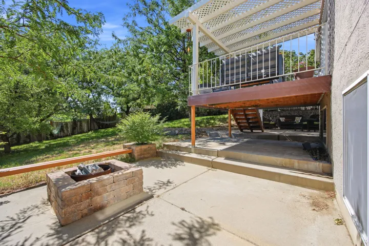 Tiered outdoor living spaces featuring a wood deck with white lattice pergola, a ground-level concrete patio, and a stone fire pit with integrated seating