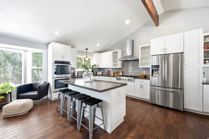 Modern kitchen featuring white cabinetry, stainless steel appliances, a center island with countertop seating, wood-finish flooring, and a vaulted ceiling with an exposed beam