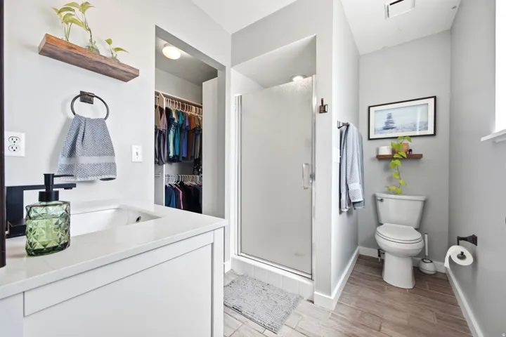 Bathroom featuring a walk-in shower with a frosted glass door, a white vanity with a light-toned countertop and integrated sink, and wood-finish flooring