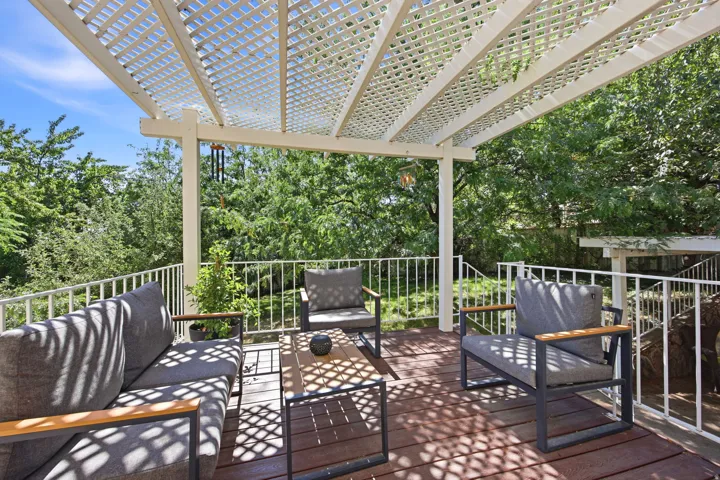 Spacious outdoor deck featuring a white lattice pergola, wood-finish flooring, and white railing