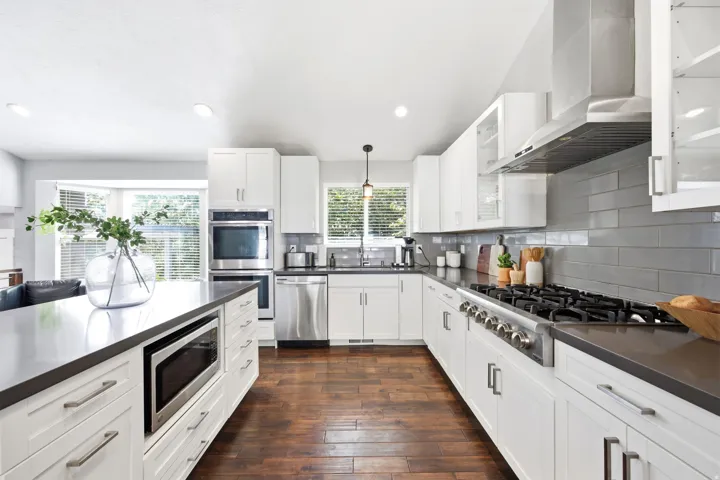 Modern kitchen featuring white cabinetry, dark countertops, wood-finish flooring, a built-in microwave drawer, and stainless steel appliances including a gas range and double wall ovens