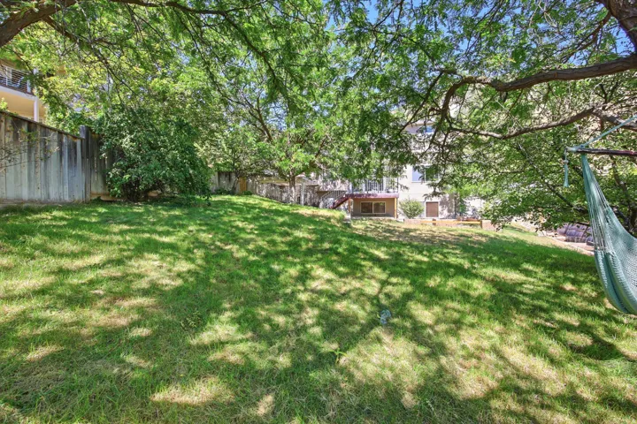 Expansive green lawn under a canopy of mature trees, featuring a concrete retaining wall and a visible portion of the property's exterior