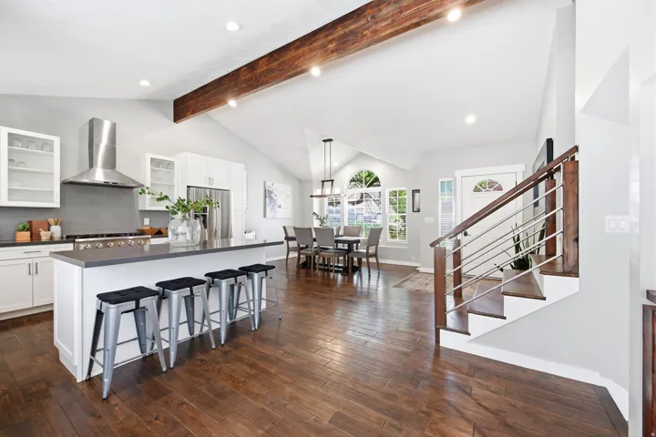 Gourmet kitchen with stainless steel appliances, a large island with seating, dark wood-finish flooring, and vaulted ceilings with exposed wood beams