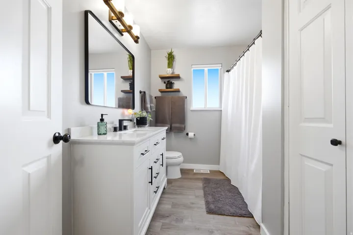 Bathroom featuring a white vanity with a light-toned countertop, a rectangular black-framed mirror, and a window with white trim