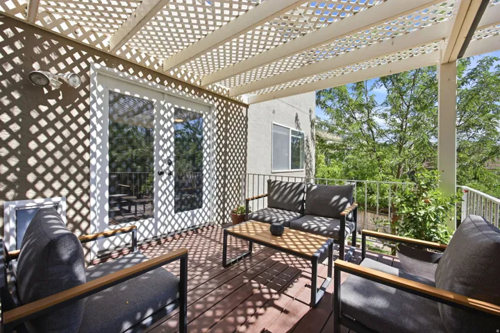 Outdoor patio featuring a lattice pergola, wood-finish decking, and white French doors