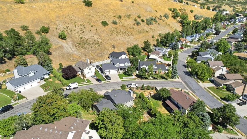 Residential neighborhood featuring varied single-family homes with mature landscaping and paved streets, set against a natural hillside backdrop