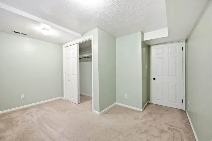 Carpeted room featuring a ceiling-mounted light fixture, light green wall paint, white trim, and a bi-fold closet door