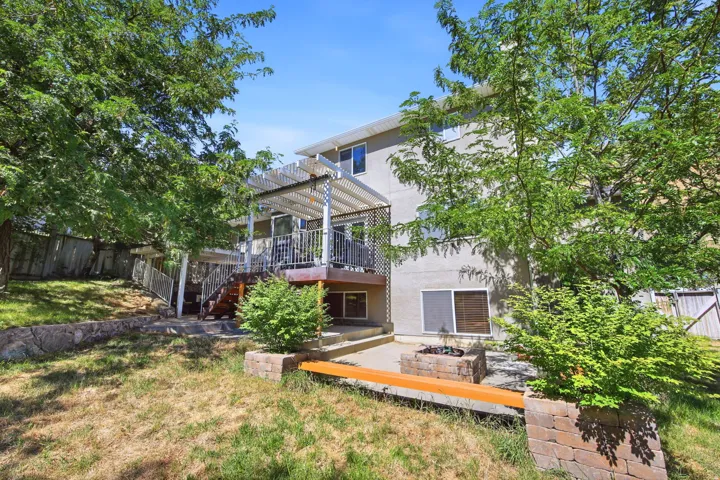 Rear exterior featuring a multi-level deck with a white lattice pergola, a ground-level patio, and a built-in fire pit with brick surround and integrated seating