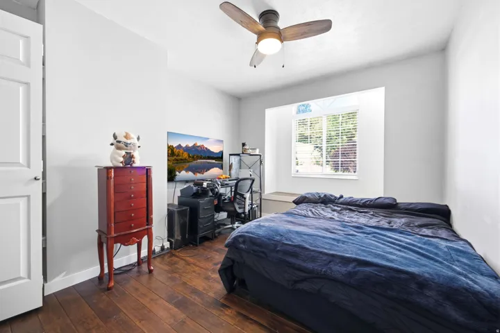 Bedroom featuring wood-finish flooring, a ceiling fan with light fixture, and a window with blinds