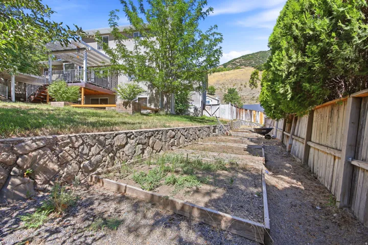 Terraced backyard featuring a stone retaining wall, raised garden beds, and a perimeter wood fence