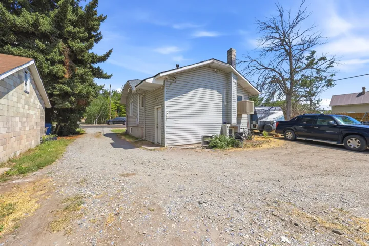Gravel driveway providing access to a light-colored siding structure with a visible chimney