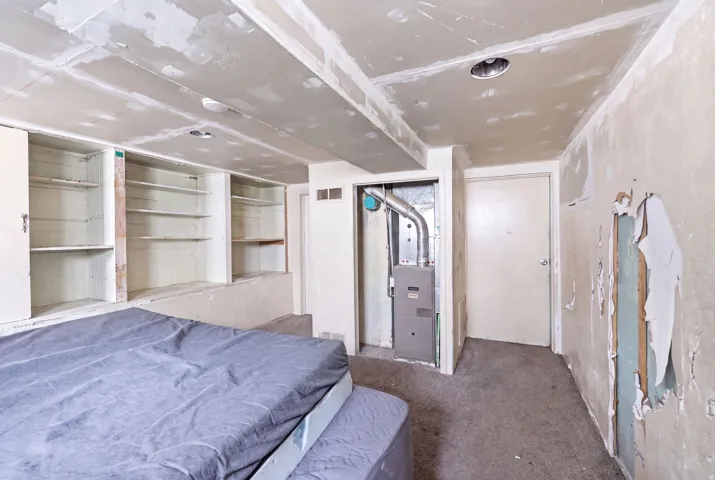 Unfinished interior space featuring built-in shelving, exposed ceiling joists, and a visible utility closet with a furnace unit