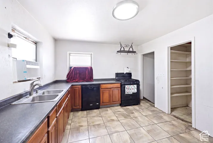Kitchen featuring a double basin stainless steel sink, wood-finish cabinetry, black appliances, and tile flooring
