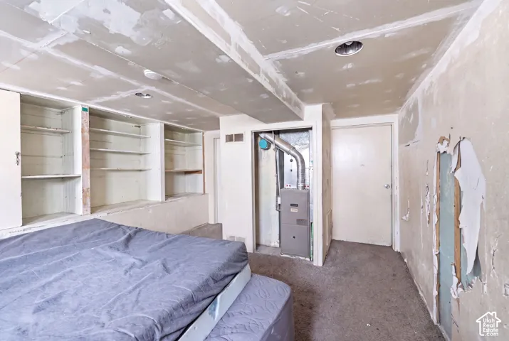 Unfinished interior space featuring built-in shelving, exposed ceiling joists, and a visible utility closet with a furnace unit