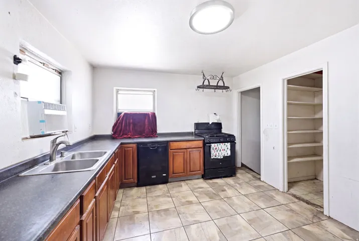 Kitchen featuring a double basin stainless steel sink, wood-finish cabinetry, black appliances, and tile flooring