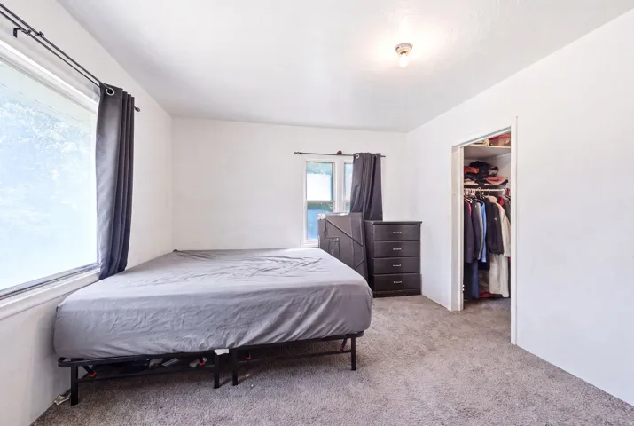 Carpeted room featuring multiple windows with dark drapery, neutral wall color, and a recessed closet with shelving and hanging space
