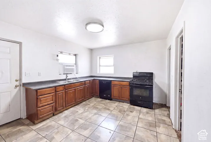 Kitchen featuring a L-shaped counter, wood-finish cabinetry, black appliances including a range and dishwasher, and tile flooring