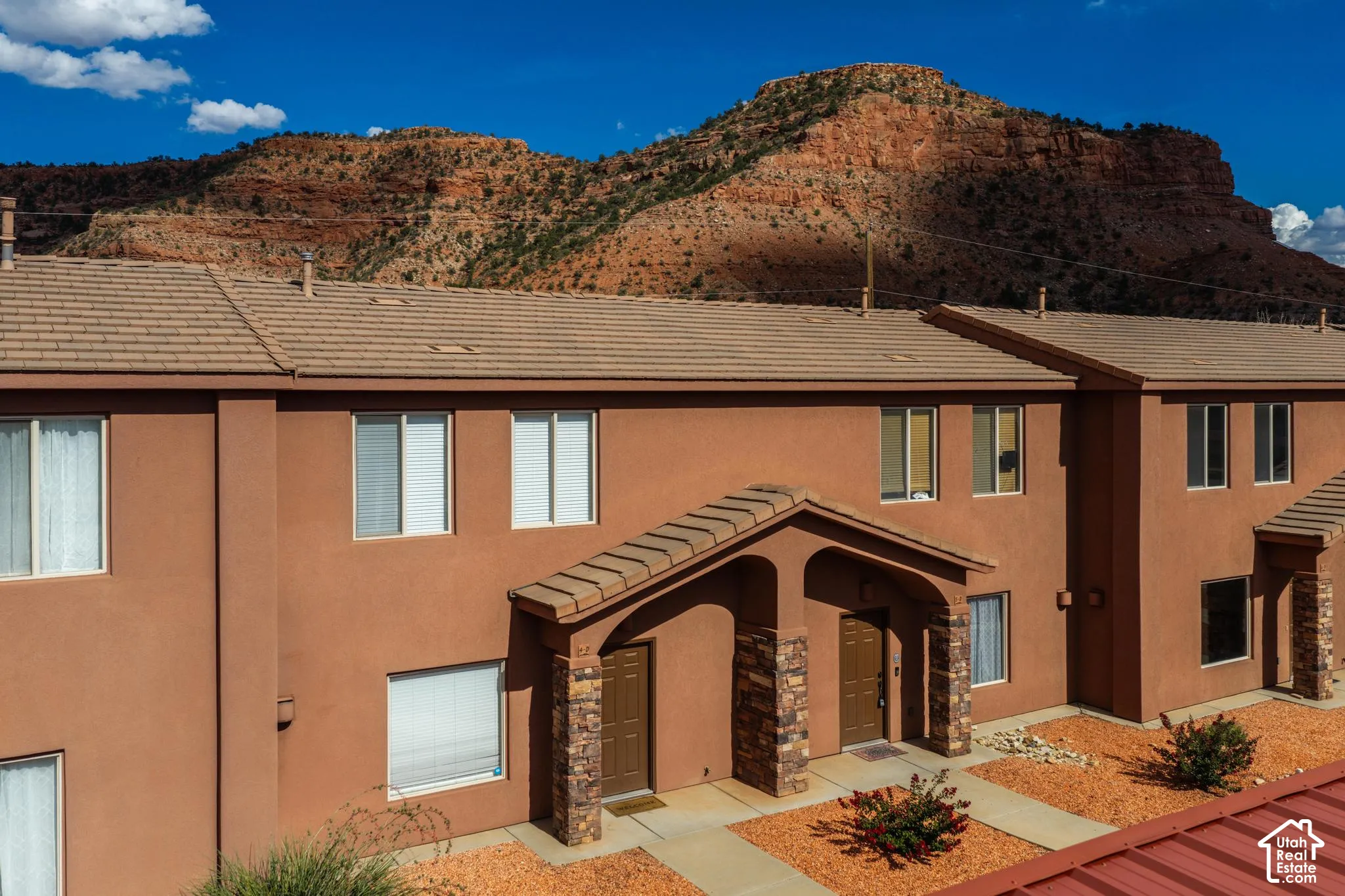 Southwestern-style multi-unit building featuring a stucco exterior, tiled roof, stone accents, covered entryways, and arid-tolerant landscaping