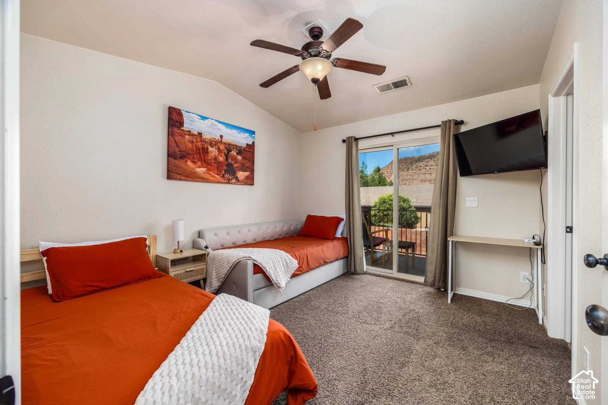 Carpeted room featuring a vaulted ceiling with a ceiling fan, sliding glass doors opening to an exterior balcony, and a mounted flat-screen display