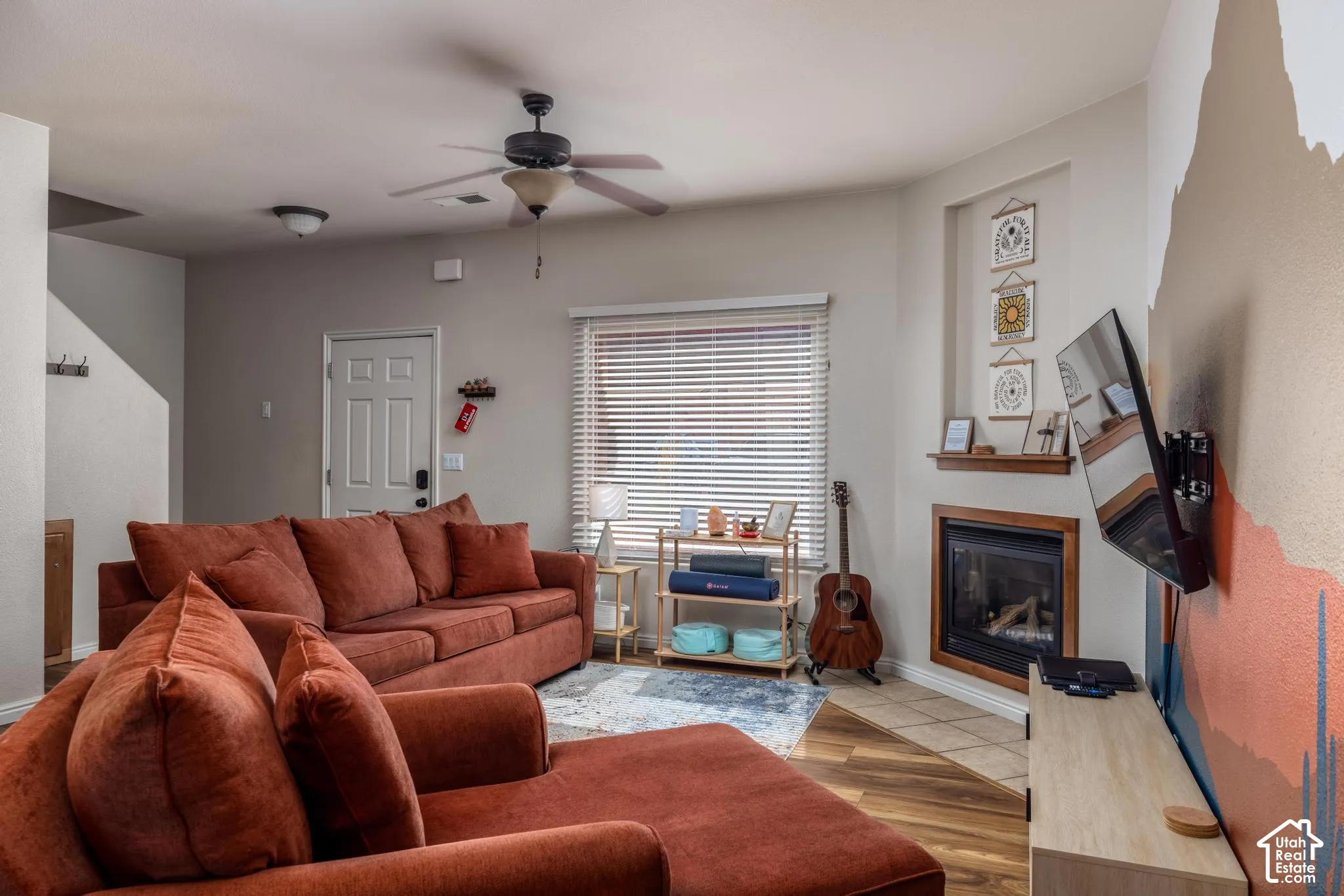 Living room featuring wood-finish flooring, a ceiling fan, and a corner-mounted fireplace with a tiled hearth and wood mantel