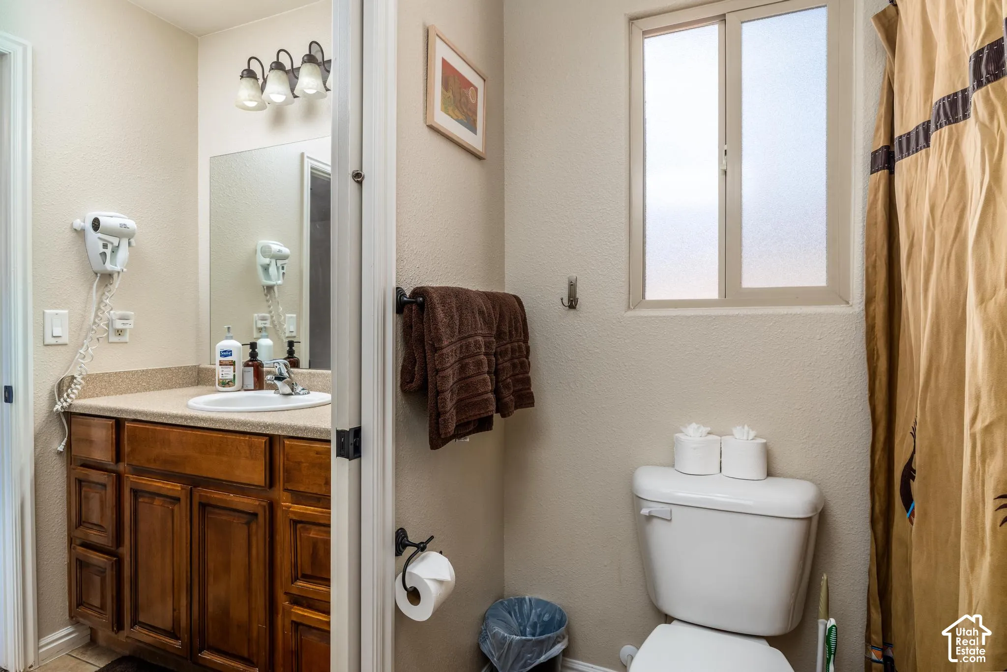 Bathroom featuring a wood-finish vanity with a built-in sink, a wall-mounted mirror, and a three-light fixture