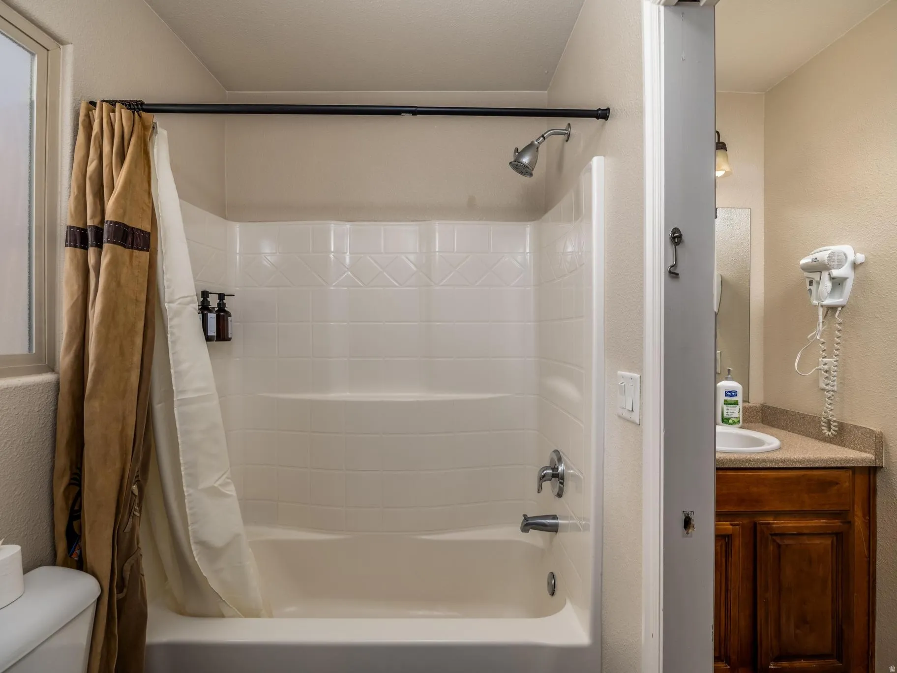 Bathroom featuring a shower/tub combination with a white surround, chrome fixtures, and an adjacent window with frosted glass