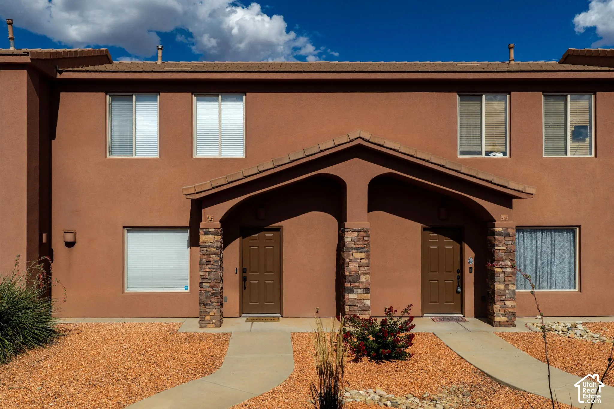 Southwestern-style facade featuring earth-toned stucco, a covered entry with stone-clad columns, tile roofing, and multiple windows