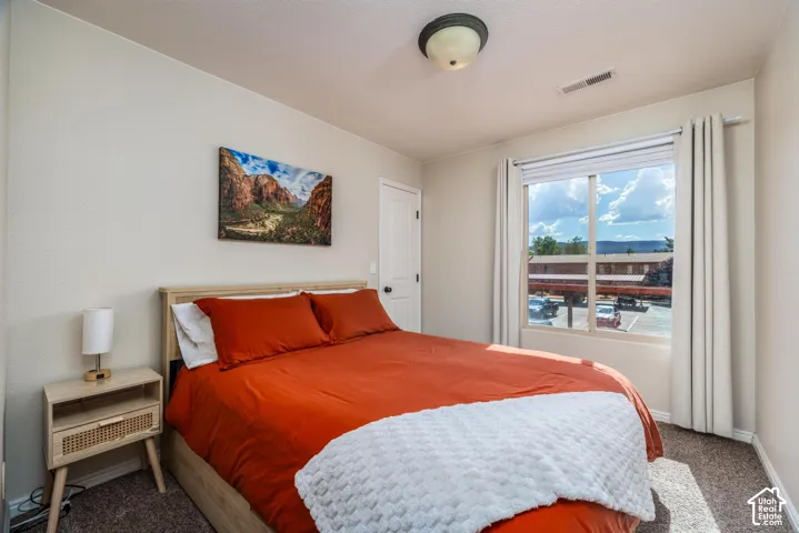 Carpeted bedroom featuring a large window with white blinds and curtains, a light-colored door, and a flush-mount ceiling light fixture